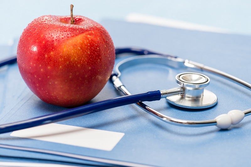 An apple resting next to a stethoscope resting on a blue folder